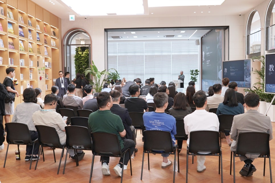 서가가 있는 행사장에서 연단의 발표를 듣는 참석자들